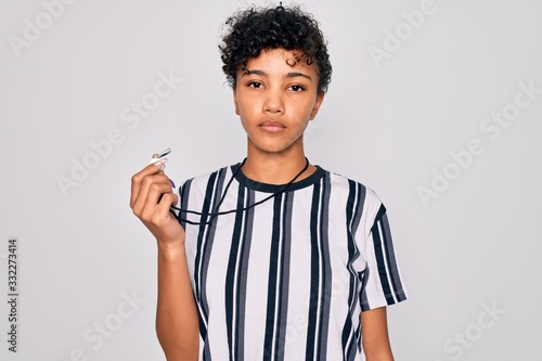 Young beautiful african american afro referee woman wearing striped uniform using whistle with a confident expression on smart face thinking serious