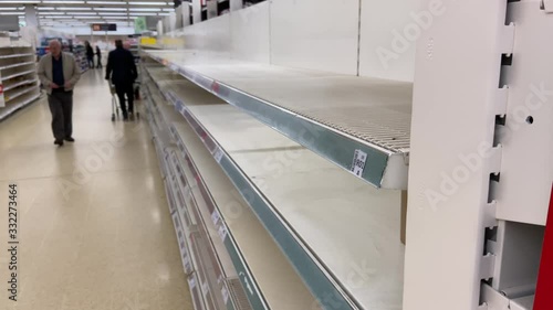 Bare supermarket empty from stockpiling. Shot of anonymous shoppers during corona virus crisis in UK retail store with empty shelves after panic buying.