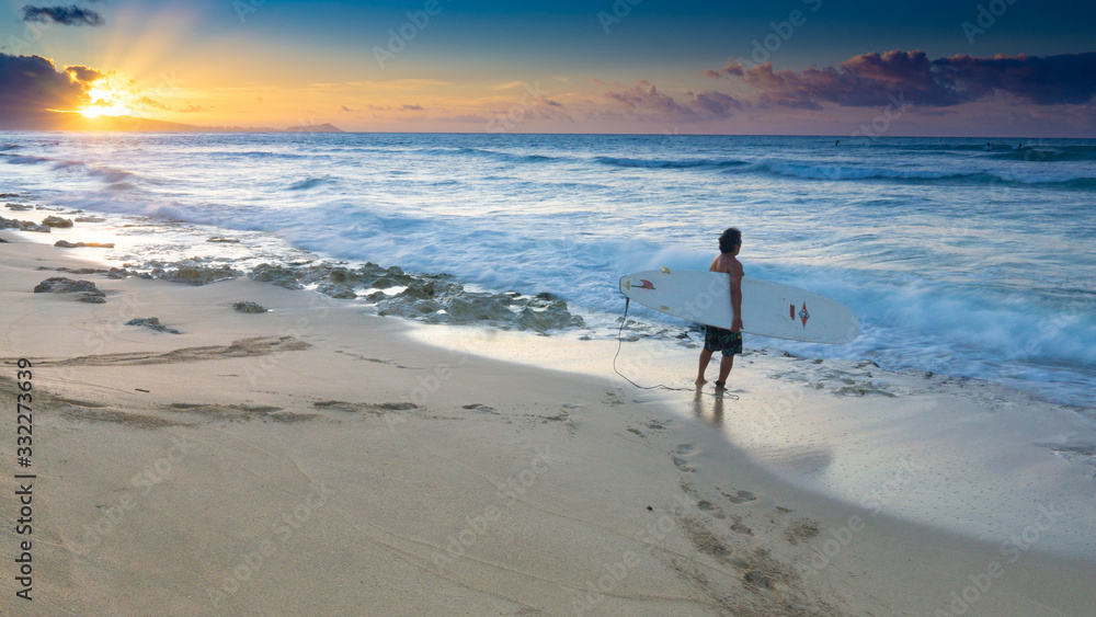 Lone surfer at a Hawaiian shore about to enter the water at sunrise Lone surfer at a Hawaiian shore about to enter the water at sunrise
