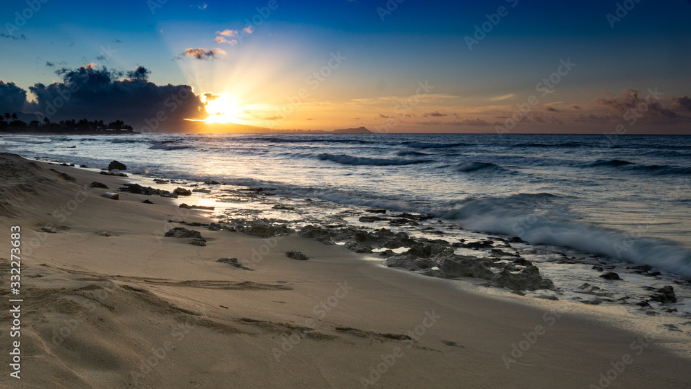 Sunrise at a Hawaiian beach with pink clouds, blue skies and golden sun.