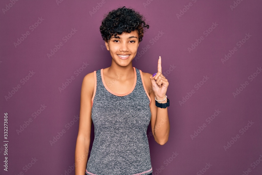 Young beautiful african american afro sportswoman doing exercise wearing sportswear showing and pointing up with finger number one while smiling confident and happy. Young beautiful african american afro sportswoman doing exercise wearing sportswear showing and pointing up with finger number one while smiling confident and happy.