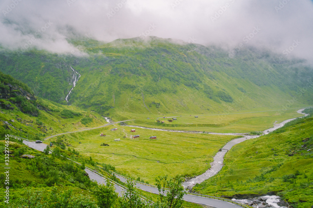 Beautiful landscape and scenery view of Norway, green scenery hills and mountain in a cloudy day. green scenery of hills and mountain partially covered with fog. Farm and cottages on a glacier river
