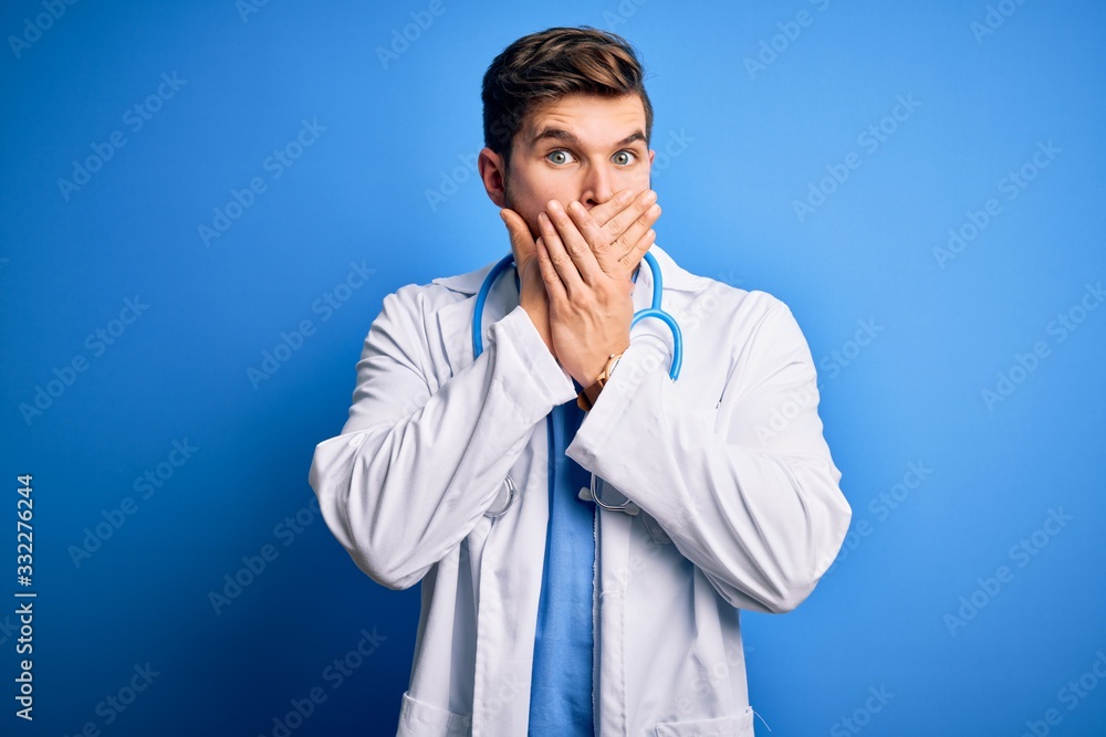 Young blond doctor man with beard and blue eyes wearing white coat and stethoscope shocked covering mouth with hands for mistake. Secret concept. Young blond doctor man with beard and blue eyes wearing white coat and stethoscope shocked covering mouth with hands for mistake. Secret concept.