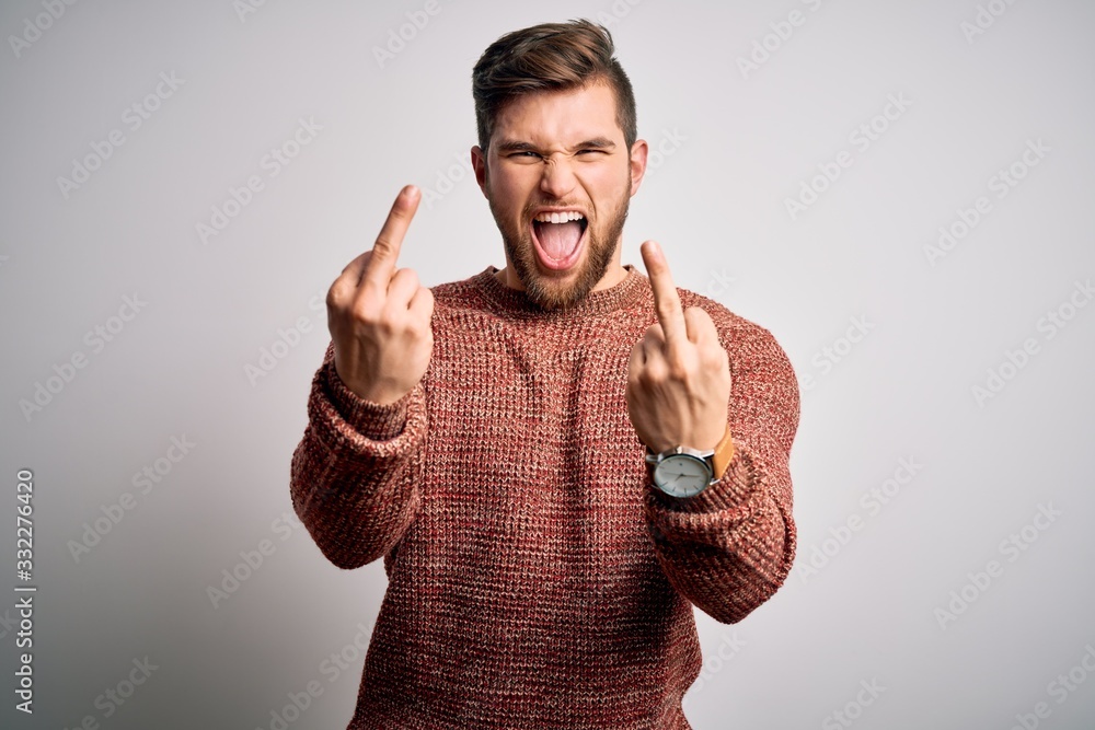 Young blond man with beard and blue eyes wearing casual sweater over white background Showing middle finger doing fuck you bad expression, provocation and rude attitude. Screaming excited Young blond man with beard and blue eyes wearing casual sweater over white background Showing middle finger doing fuck you bad expression, provocation and rude attitude. Screaming excited