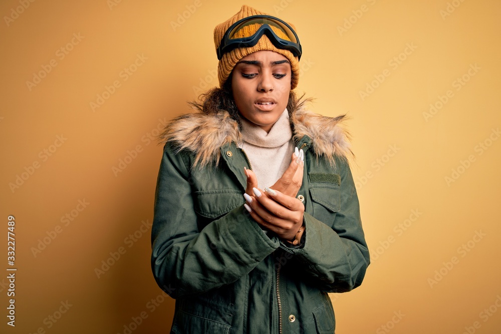 Young african american afro skier girl wearing snow sportswear and ski goggles Suffering pain on hands and fingers, arthritis inflammation Young african american afro skier girl wearing snow sportswear and ski goggles Suffering pain on hands and fingers, arthritis inflammation
