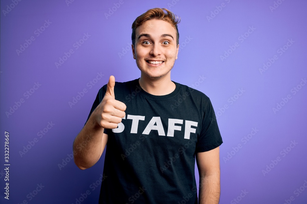 Young handsome redhead worker man wearing staff t-shirt uniform over purple background doing happy thumbs up gesture with hand. Approving expression looking at the camera showing success. Young handsome redhead worker man wearing staff t-shirt uniform over purple background doing happy thumbs up gesture with hand. Approving expression looking at the camera showing success.