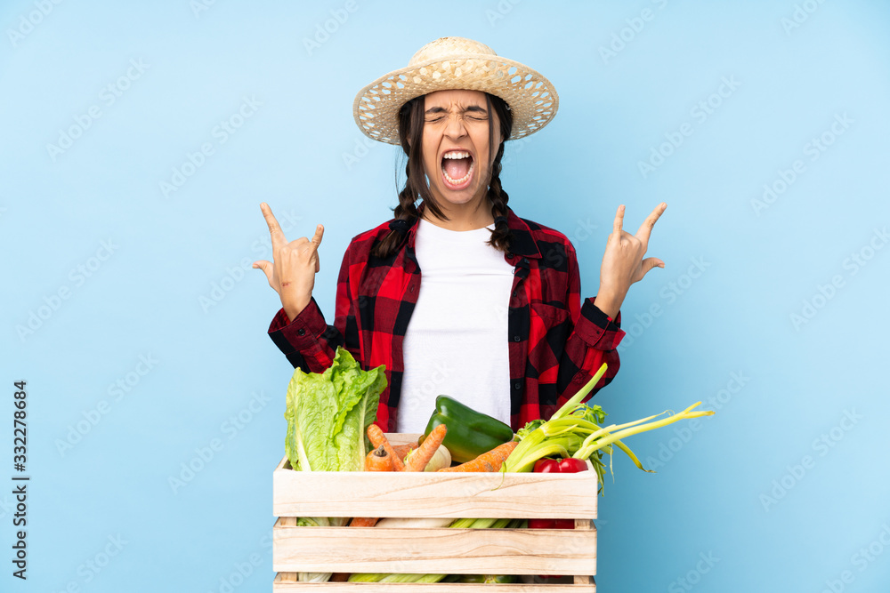 Young farmer Woman holding fresh vegetables in a wooden basket making rock gesture