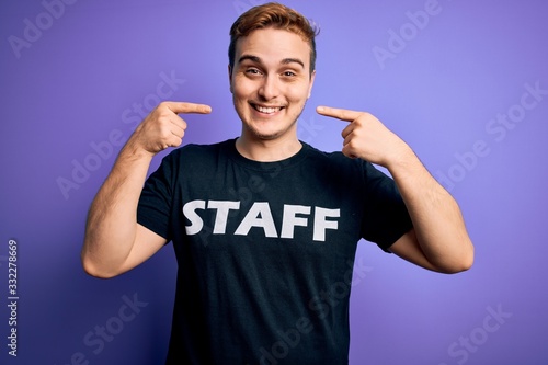 Young handsome redhead worker man wearing staff t-shirt uniform over purple background smiling cheerful showing and pointing with fingers teeth and mouth. Dental health concept. © Krakenimages.com