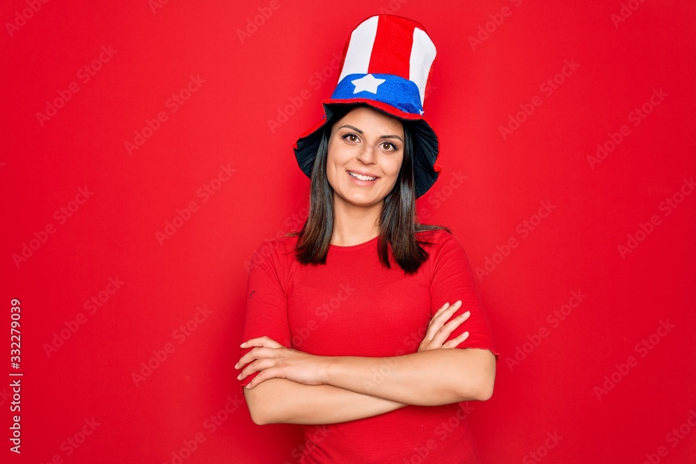 Young beautiful brunette woman wearing united states hat celebrating independence day happy face smiling with crossed arms looking at the camera. Positive person. Young beautiful brunette woman wearing united states hat celebrating independence day happy face smiling with crossed arms looking at the camera. Positive person.