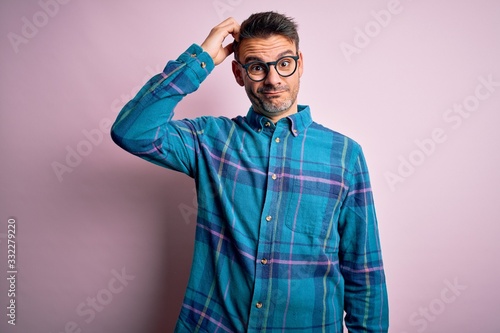 Young handsome man wearing casual shirt and glasses standing over isolated pink background confuse and wonder about question. Uncertain with doubt, thinking with hand on head. Pensive concept. © Krakenimages.com