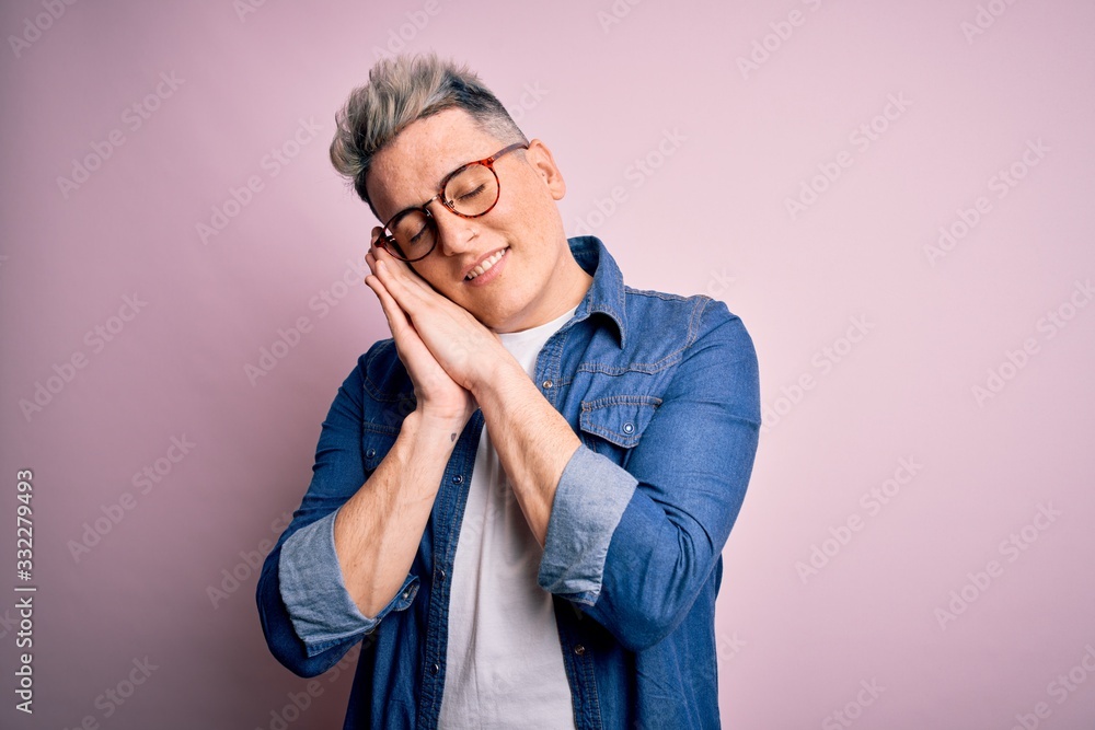 Young handsome modern man wearing glasses and denim jacket over pink isolated background sleeping tired dreaming and posing with hands together while smiling with closed eyes. Young handsome modern man wearing glasses and denim jacket over pink isolated background sleeping tired dreaming and posing with hands together while smiling with closed eyes.