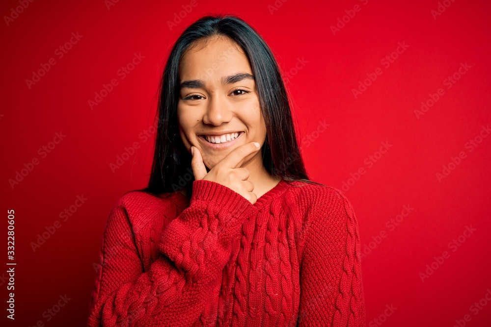 Fototapeta premium Young beautiful asian woman wearing casual sweater standing over isolated red background looking confident at the camera smiling with crossed arms and hand raised on chin. Thinking positive.