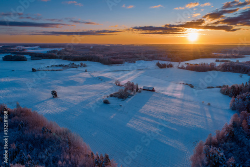 Aerial view of beautiful sunrise above snowy field with an old barn with long shadows.