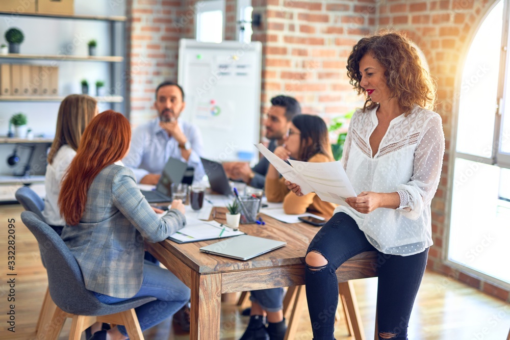 Fototapeta premium Group of business workers working together. Middle age beautiful businesswoman standing smiling happy looking at the camera at the office