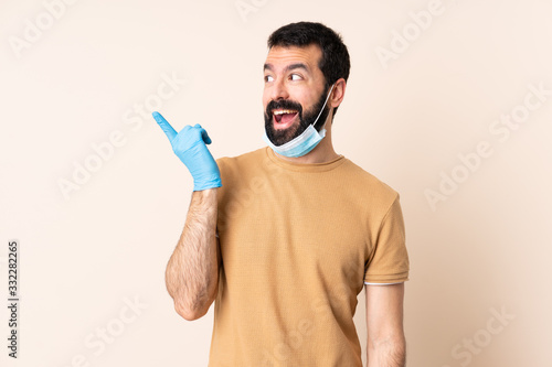 Caucasian man with beard protecting from the coronavirus with a mask and gloves over isolated background intending to realizes the solution while lifting a finger up