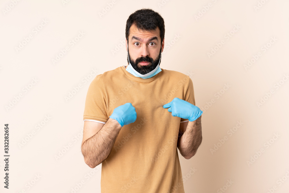 Caucasian man with beard protecting from the coronavirus with a mask and gloves over isolated background pointing to oneself Caucasian man with beard protecting from the coronavirus with a mask and gloves over isolated background pointing to oneself