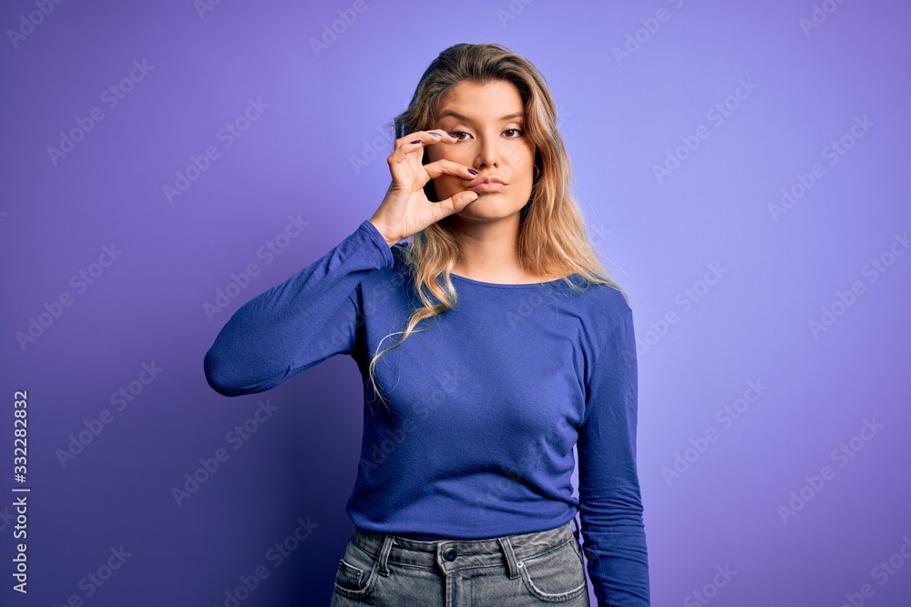 Young beautiful blonde woman wearing casual t-shirt over isolated purple background mouth and lips shut as zip with fingers. Secret and silent, taboo talking Young beautiful blonde woman wearing casual t-shirt over isolated purple background mouth and lips shut as zip with fingers. Secret and silent, taboo talking