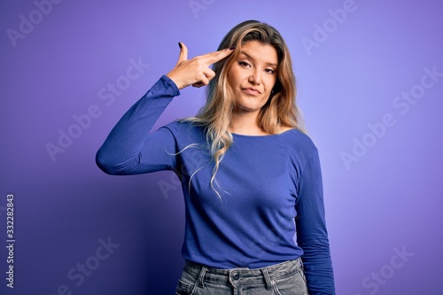 Young beautiful blonde woman wearing casual t-shirt over isolated purple background Shooting and killing oneself pointing hand and fingers to head like gun, suicide gesture.