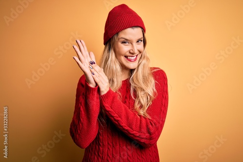 Young beautiful blonde woman wearing casual sweater and wool cap over white background clapping and applauding happy and joyful, smiling proud hands together