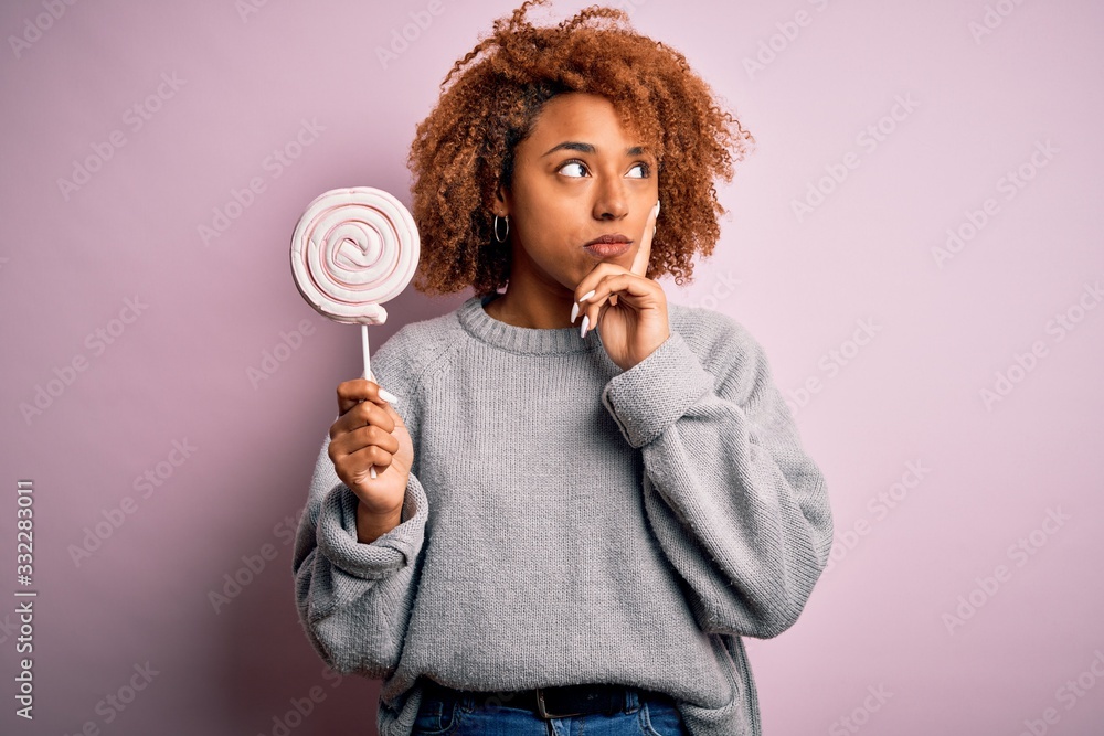 Young beautiful African American afro woman with curly hair eating sweet candy serious face thinking about question, very confused idea Young beautiful African American afro woman with curly hair eating sweet candy serious face thinking about question, very confused idea