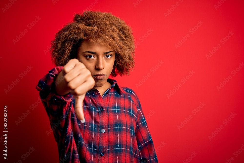 Young beautiful African American afro woman with curly hair wearing casual shirt looking unhappy and angry showing rejection and negative with thumbs down gesture. Bad expression. Young beautiful African American afro woman with curly hair wearing casual shirt looking unhappy and angry showing rejection and negative with thumbs down gesture. Bad expression.