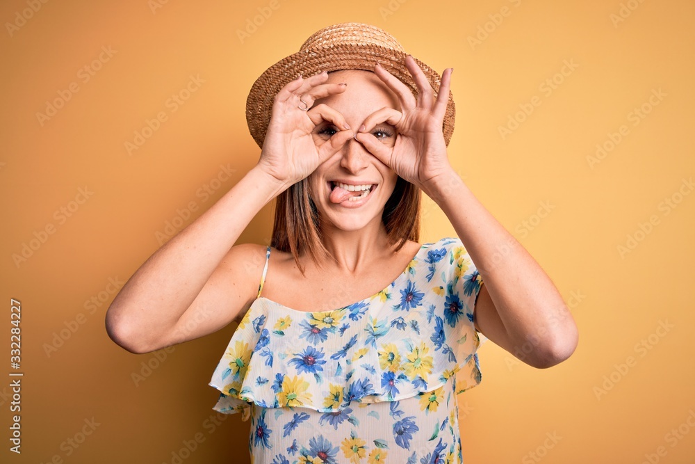 Young beautiful woman wearing casual t-shirt and summer hat over isolated yellow background doing ok gesture like binoculars sticking tongue out, eyes looking through fingers. Crazy expression. Young beautiful woman wearing casual t-shirt and summer hat over isolated yellow background doing ok gesture like binoculars sticking tongue out, eyes looking through fingers. Crazy expression.