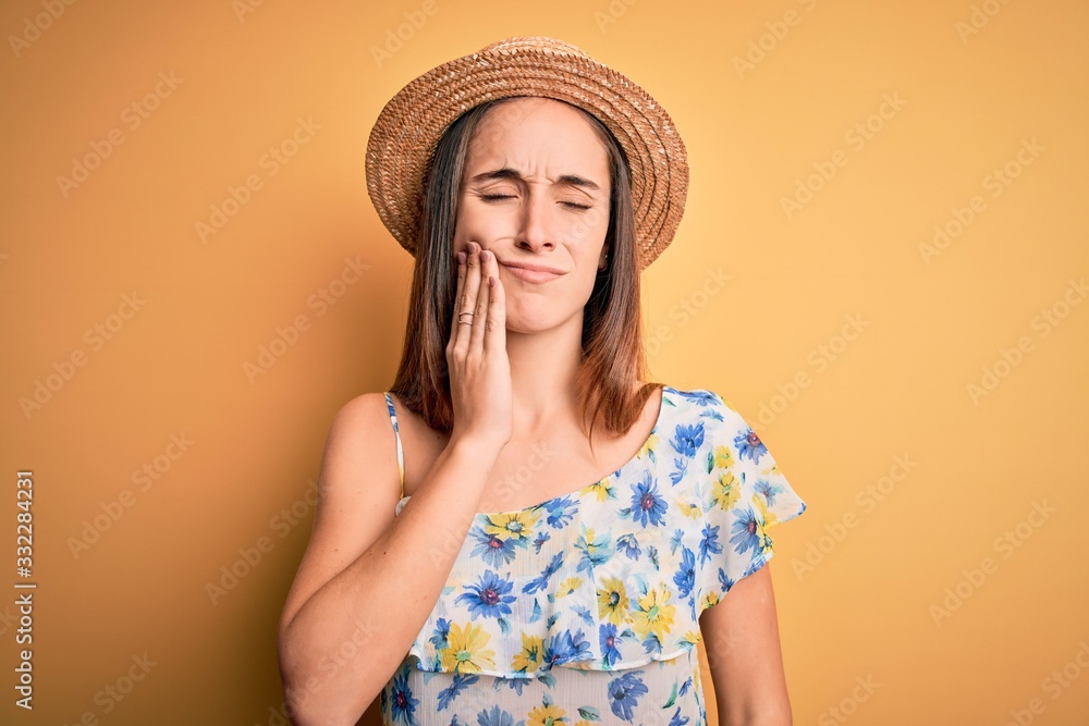 Young beautiful woman wearing casual t-shirt and summer hat over isolated yellow background touching mouth with hand with painful expression because of toothache or dental illness on teeth. Dentist Young beautiful woman wearing casual t-shirt and summer hat over isolated yellow background touching mouth with hand with painful expression because of toothache or dental illness on teeth. Dentist
