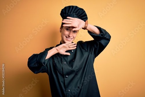 Young beautiful chef woman wearing cooker uniform and hat standing over yellow background Smiling cheerful playing peek a boo with hands showing face. Surprised and exited © Krakenimages.com