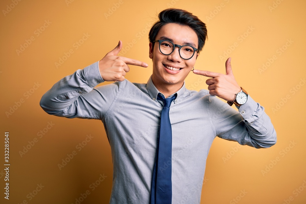 Young handsome chinese businessman wearing glasses and tie over yellow background smiling cheerful showing and pointing with fingers teeth and mouth. Dental health concept. Young handsome chinese businessman wearing glasses and tie over yellow background smiling cheerful showing and pointing with fingers teeth and mouth. Dental health concept.