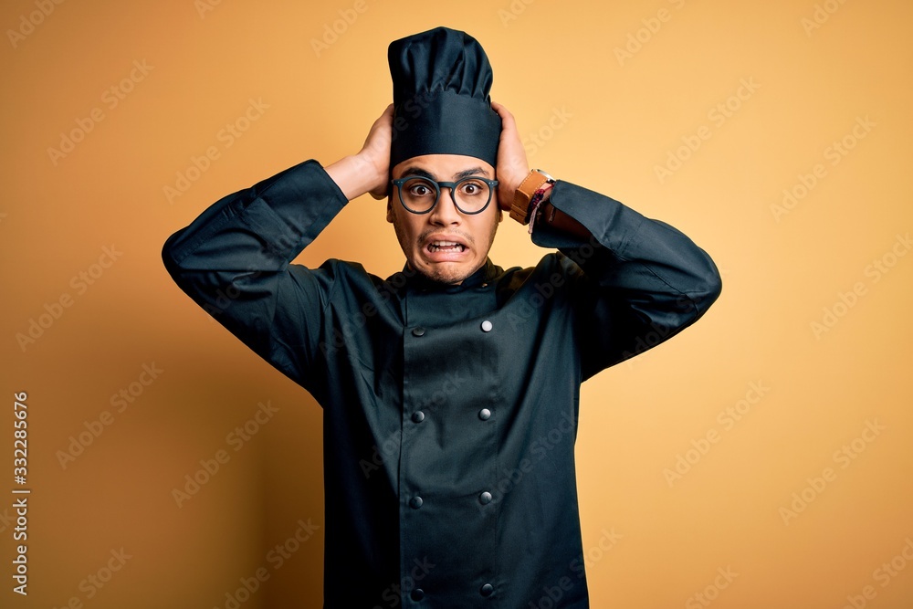 Young brazilian chef man wearing cooker uniform and hat over isolated yellow background Crazy and scared with hands on head, afraid and surprised of shock with open mouth Young brazilian chef man wearing cooker uniform and hat over isolated yellow background Crazy and scared with hands on head, afraid and surprised of shock with open mouth