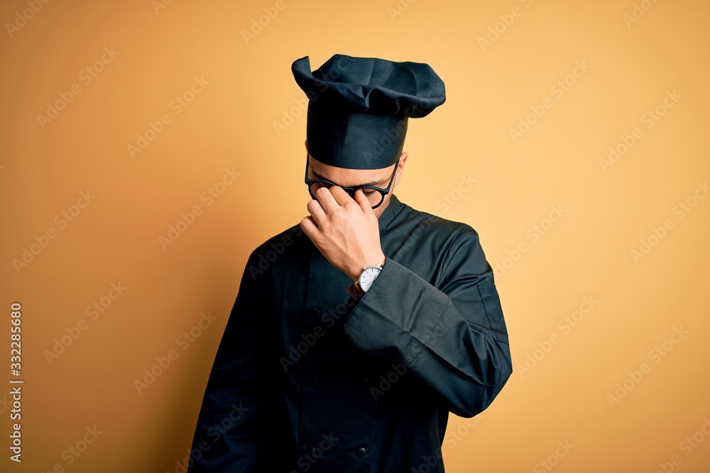 Young brazilian chef man wearing cooker uniform and hat over isolated yellow background tired rubbing nose and eyes feeling fatigue and headache. Stress and frustration concept.