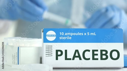 Box with placebo medicine on the table against blurred lab assistant. Fictional phaceutical logo photo