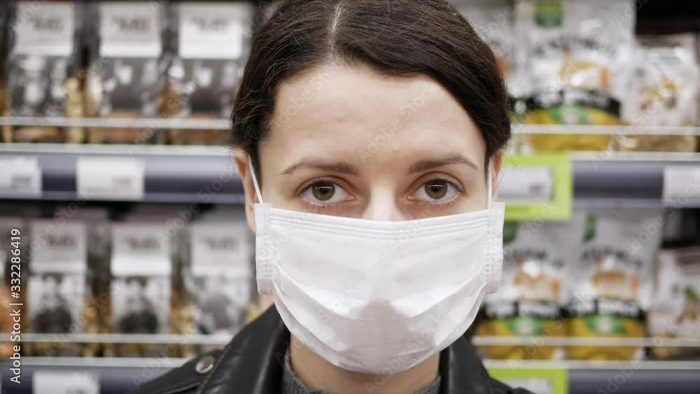 Portrait of young woman in medical mask stands in supermarket. Protection from coronavirus, purchase of food for quarantine. Deficit of products Portrait of young woman in medical mask stands in supermarket. Protection from coronavirus, purchase of food for quarantine. Deficit of products