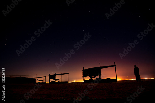 A man watches the starry night on a beach and surrounded by wooden huts to chill out