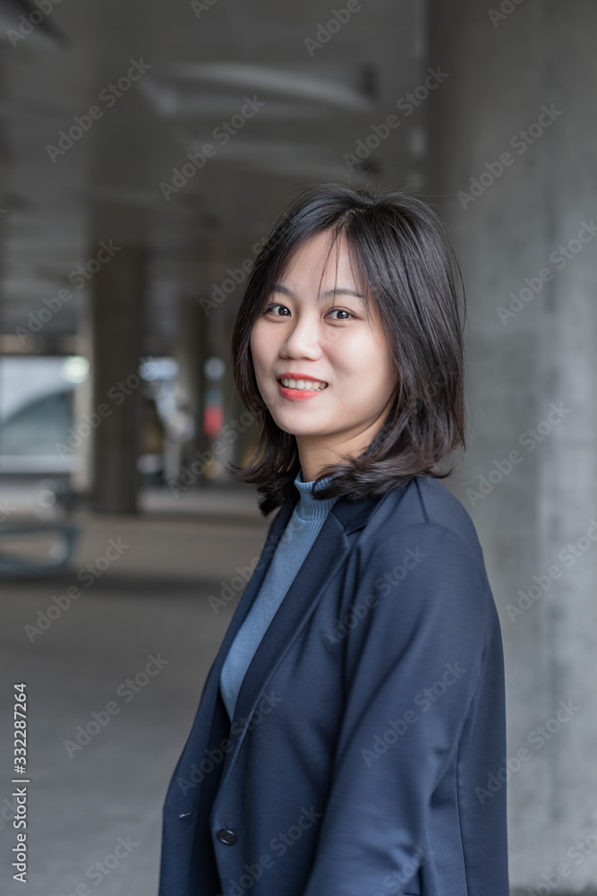 In front of the gray wall, young business women smile to the camera