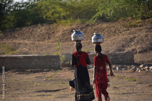 インドのラジャスタン州 ジャイサルメールのクーリー村 水瓶を頭に乗せて運ぶ、インド人女性 民族衣装のサリーを着て働く、美しい姿