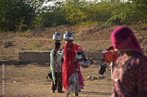 インドのラジャスタン州 ジャイサルメールのクーリー村 水瓶を頭に乗せて運ぶ、インド人女性 民族衣装のサリーを着て働く、美しい姿