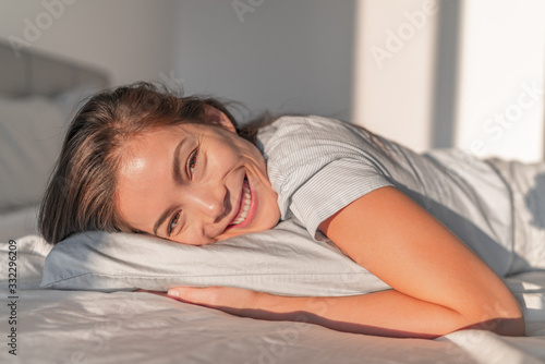 Happy home relaxation asian smiling woman staying in bed relaxing in bedroom candid portrait. Natural beauty healthy skincare model face. Comfortable foam mattress and pillow.