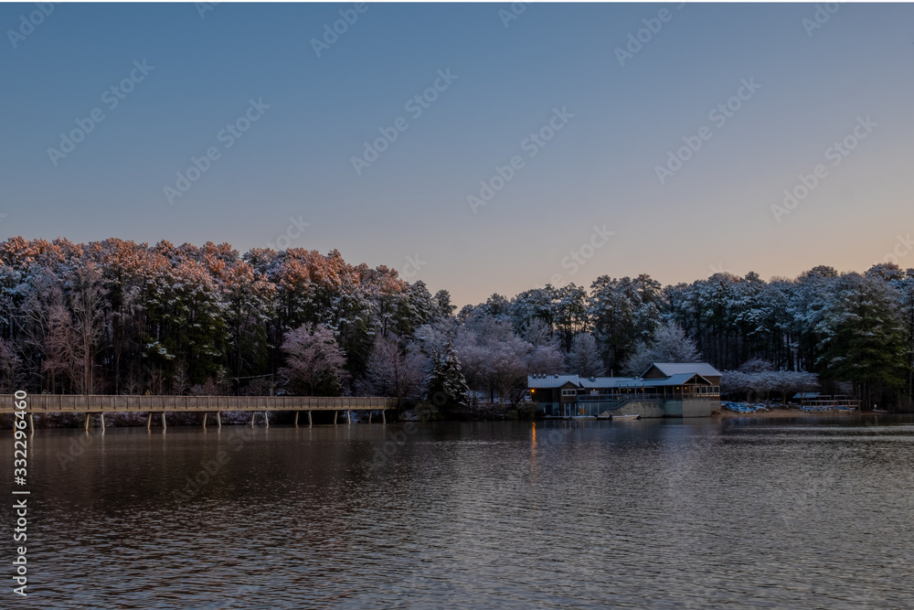 Early morning sunlight striking the snow-covered treetops by the boathouse at Lake Johnson Park in Raleigh, North Carolina.