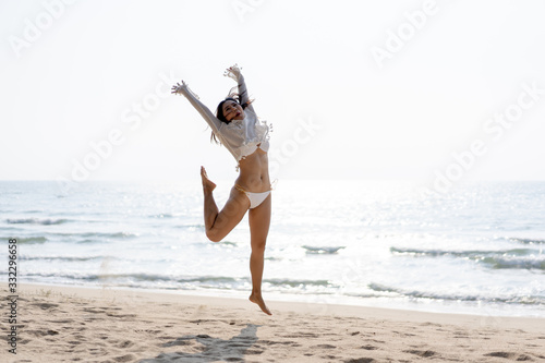 Happy young woman in bikini jumping on the beach