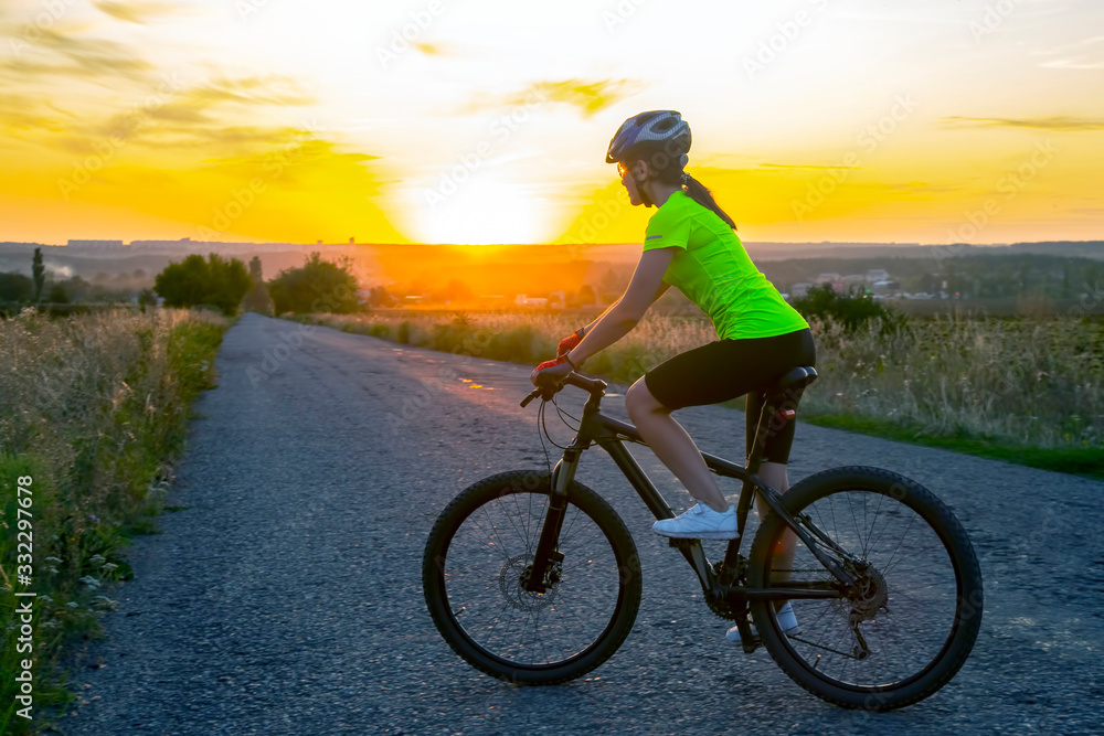 Beautiful girl cyclist riding a bike on the road towards the sunset. Nature and recreation. Hobbies and sports Beautiful girl cyclist riding a bike on the road towards the sunset. Nature and recreation. Hobbies and sports