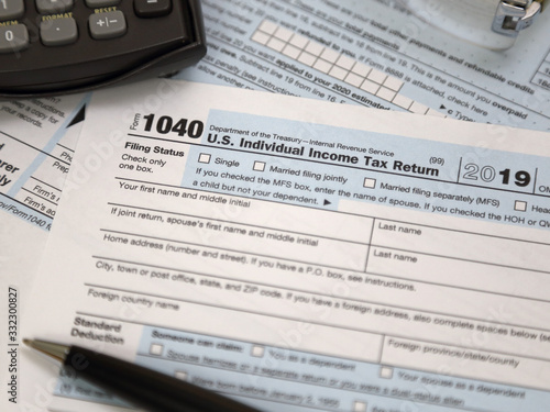 An IRS 1040 tax year 2019 form is shown in 2020, along with an ink pen, calculator, and glasses. The Internal Revenue Service tax filing deadline has been extended from April 15 to July 15 this year.
