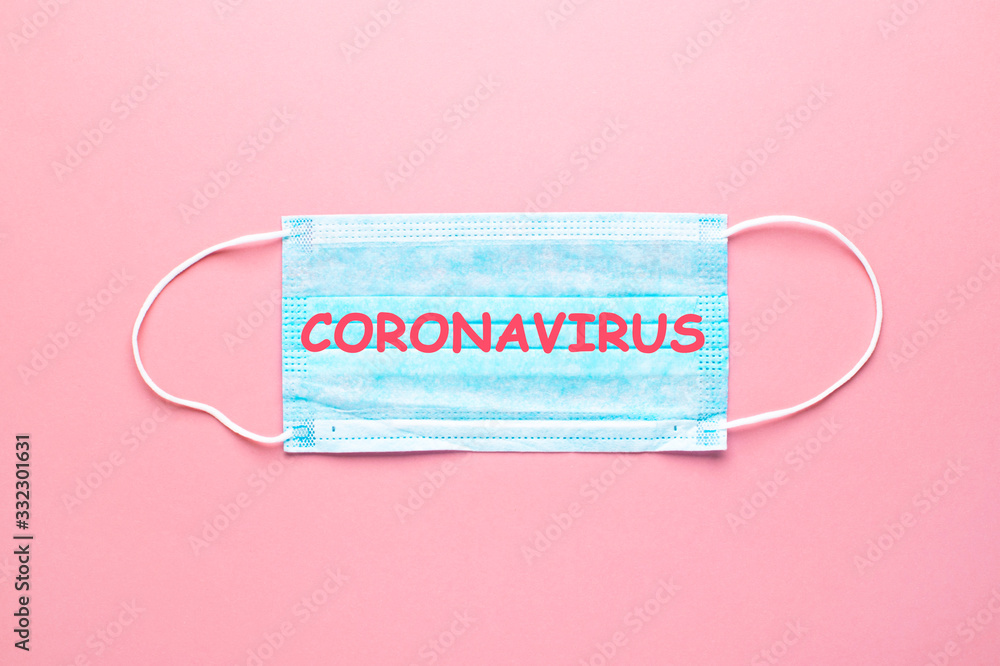 Medical protective face mask at pink background. Word Coronavirus with red letters at mask. Medical protective face mask at pink background. Word Coronavirus with red letters at mask.