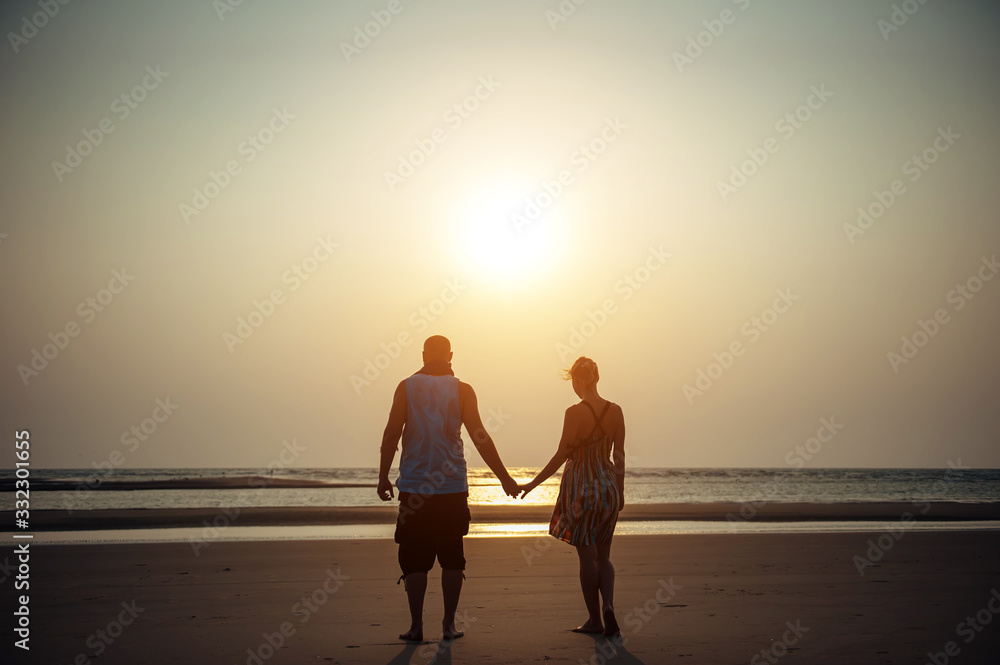 Silhouettes of man and woman on the background of the sea in the rays of setting sun. Young couple in love holding hands at sunset. Concept of love, family, relationships. Romance, honeymoon.