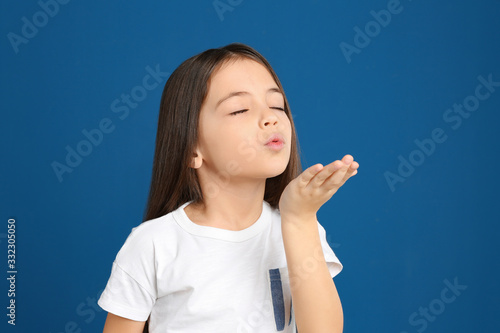 Cute little girl blowing kiss on blue background