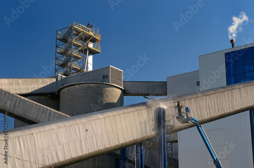 Worker on a boom truck lift powerwashing a outdoor conveyor chute at an industrial complex