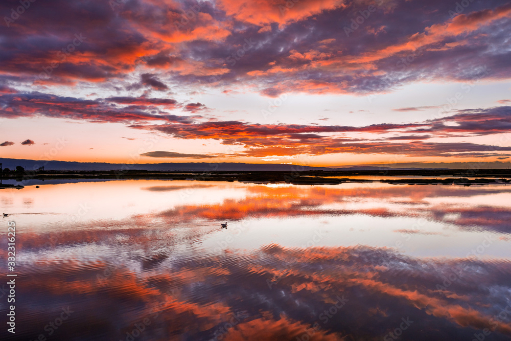 Sunset views of the tidal marshes of Alviso with colorful clouds reflected on the calm water surface, Don Edwards San Francisco Bay National Wildlife Refuge, San Jose, California