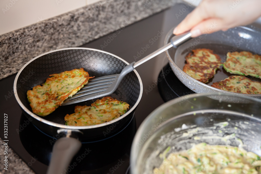 Process frying zucchini pancakes in frying pan in kitchen
