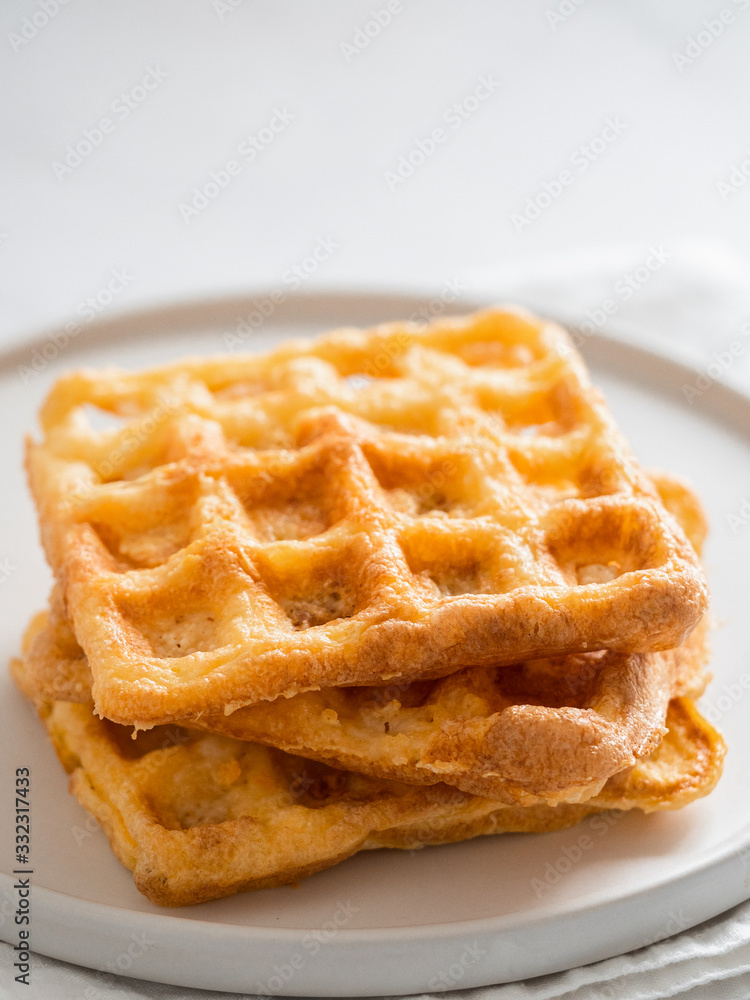 Perfect savory keto waffles. Two ingredients chaffles on plate over white marble background. Eggs and parmesan cheese low carb waffles. Extreme close up view. Vertical. Perfect savory keto waffles. Two ingredients chaffles on plate over white marble background. Eggs and parmesan cheese low carb waffles. Extreme close up view. Vertical.
