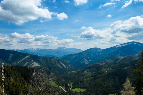 A vast view on Alpine valley from the upper parts of Himmeleck in Austria. The valley is lush green. There are many mountain ranges in the back. Spring coming to the Alps. Dense forest © Chris